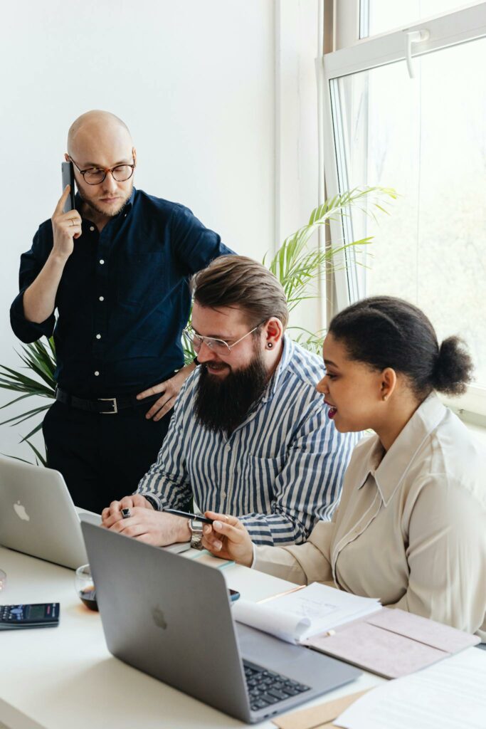A diverse group of professionals engaged in a collaborative team meeting at a modern office with laptops and mobile phones.